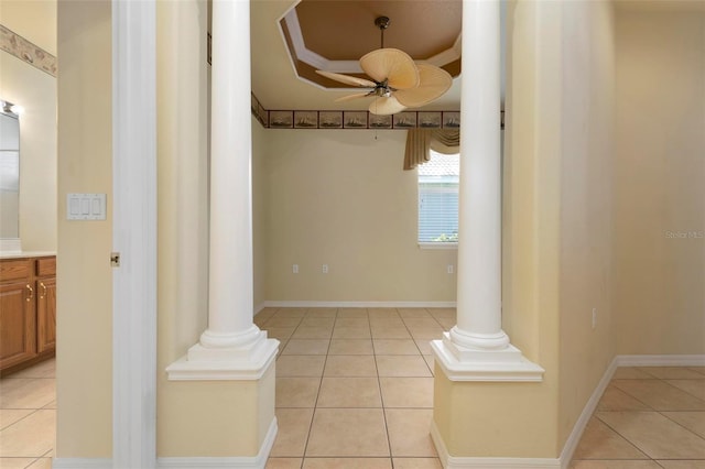 corridor with a tray ceiling, ornate columns, and light tile patterned floors