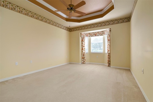 empty room with carpet floors, ceiling fan, a raised ceiling, and crown molding