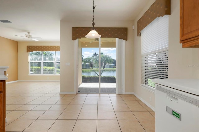 unfurnished dining area with a water view, light tile patterned floors, and ceiling fan