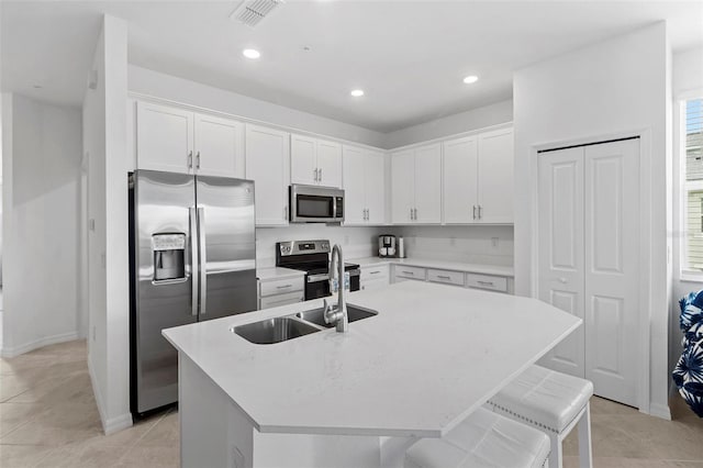 kitchen featuring a breakfast bar area, an island with sink, white cabinets, appliances with stainless steel finishes, and light tile patterned floors