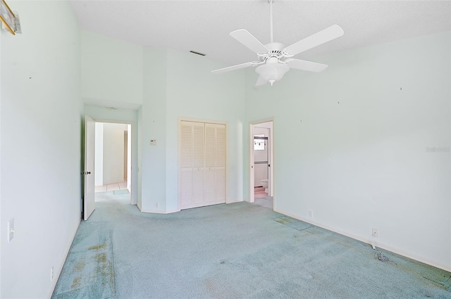 unfurnished bedroom featuring ceiling fan, connected bathroom, a closet, a towering ceiling, and light colored carpet