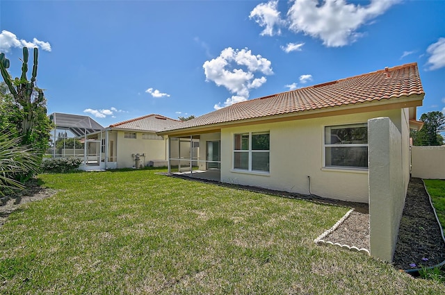 rear view of property featuring a yard, a tile roof, and stucco siding