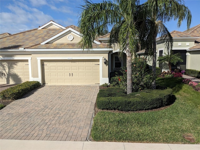 view of front of house with decorative driveway, a tile roof, stucco siding, an attached garage, and a front lawn