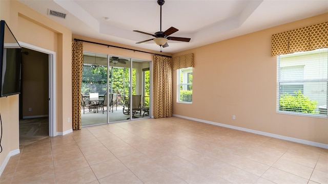 empty room featuring a tray ceiling, visible vents, and baseboards