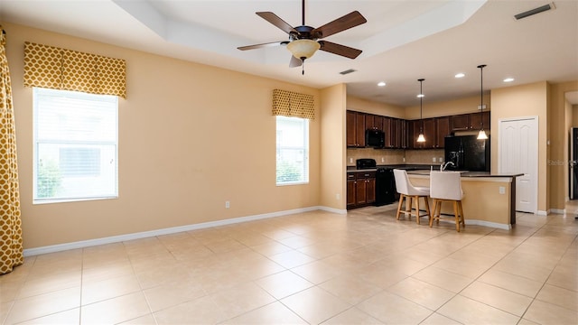 kitchen featuring a breakfast bar, a center island with sink, a raised ceiling, backsplash, and black appliances