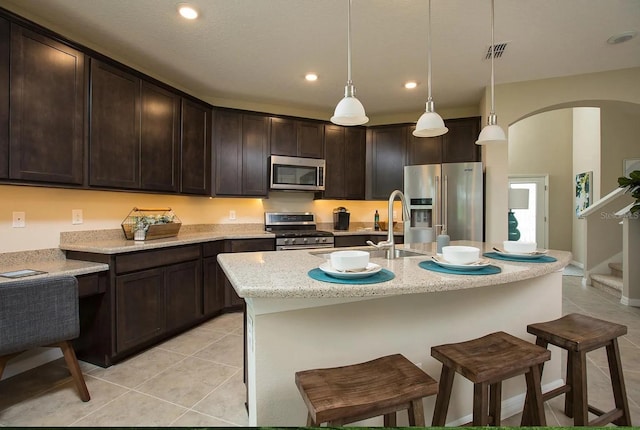 kitchen with light tile patterned flooring, appliances with stainless steel finishes, light stone counters, and decorative light fixtures