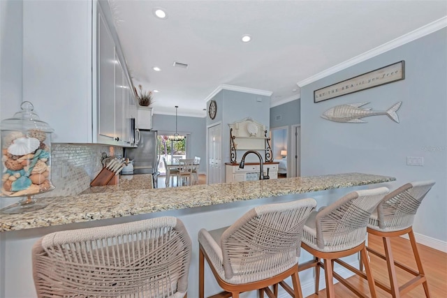 kitchen with light wood-type flooring, kitchen peninsula, and ornamental molding