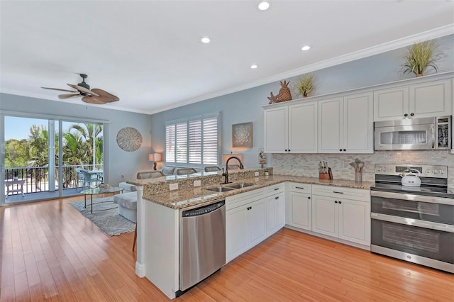 kitchen with appliances with stainless steel finishes, white cabinets, kitchen peninsula, and light wood-type flooring