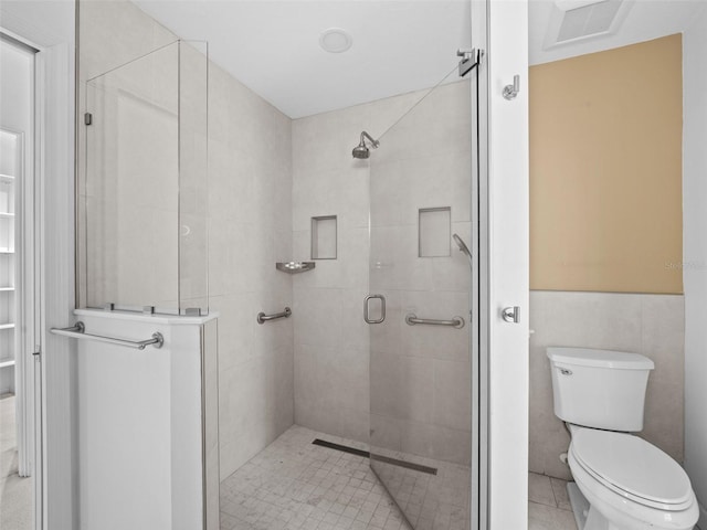 bathroom with tile patterned flooring, toilet, a shower with door, and tile walls