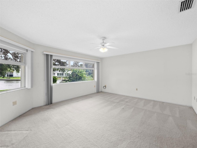 spare room with ceiling fan, plenty of natural light, light colored carpet, and a textured ceiling