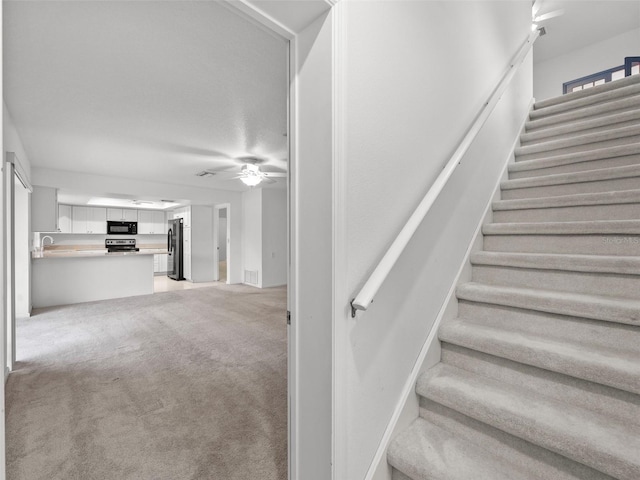 stairway featuring ceiling fan, sink, and light colored carpet