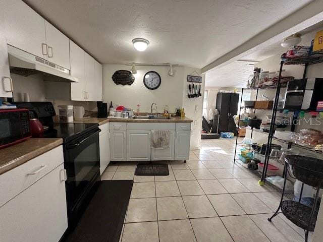 kitchen with sink, black appliances, light tile patterned floors, and white cabinets