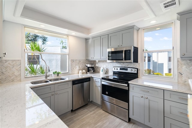 kitchen with stainless steel appliances, gray cabinets, light stone countertops, and sink