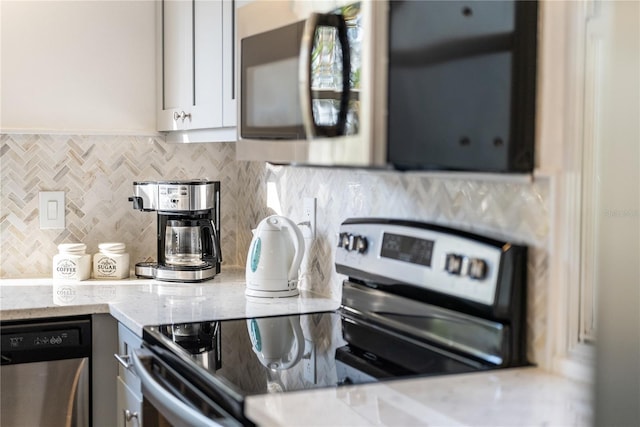 kitchen with gray cabinets, stainless steel appliances, light stone countertops, white cabinets, and decorative backsplash