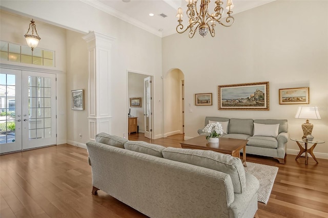 living room with french doors, an inviting chandelier, ornate columns, and hardwood / wood-style floors