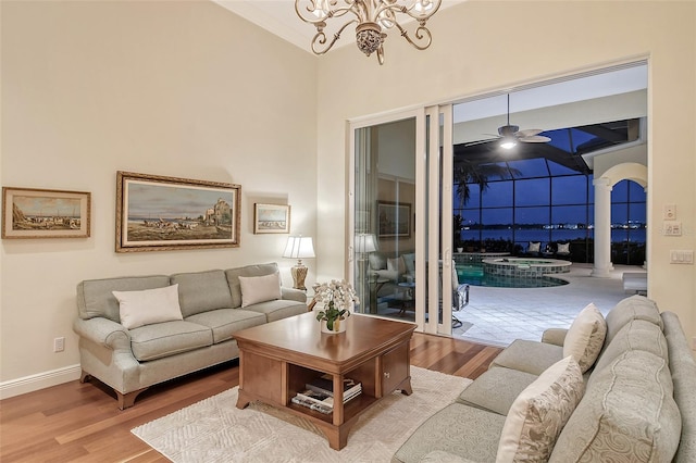 living room with a high ceiling, light hardwood / wood-style floors, and ceiling fan with notable chandelier