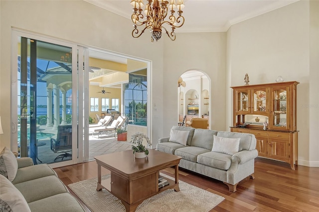 living room with wood-type flooring, ceiling fan with notable chandelier, built in features, and crown molding