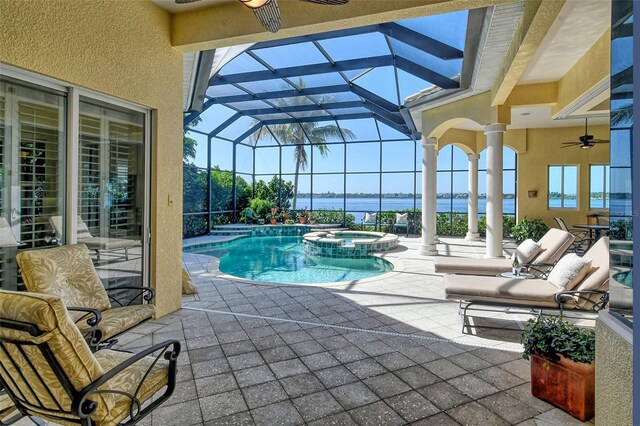 view of pool featuring glass enclosure, a water view, ceiling fan, an in ground hot tub, and a patio area