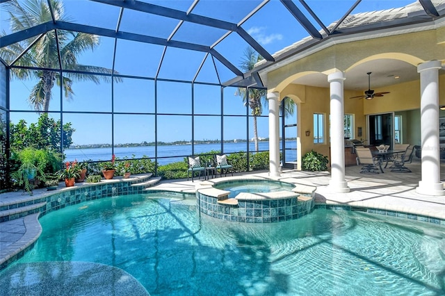 view of pool with glass enclosure, ceiling fan, exterior kitchen, an in ground hot tub, and a water view