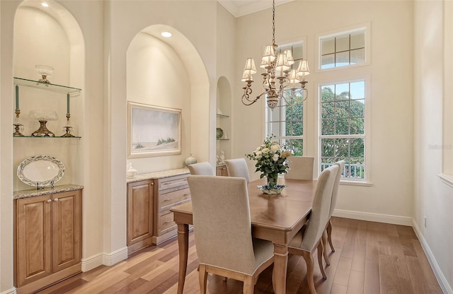 dining room featuring a notable chandelier, built in shelves, light wood-type flooring, and a high ceiling