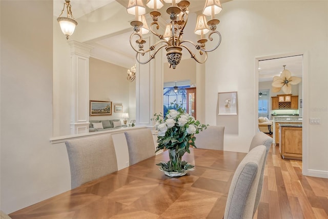 dining area featuring decorative columns, beamed ceiling, light wood-type flooring, and a notable chandelier