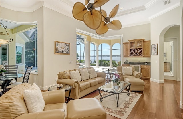 living room featuring bar area, ceiling fan, light hardwood / wood-style flooring, and ornamental molding