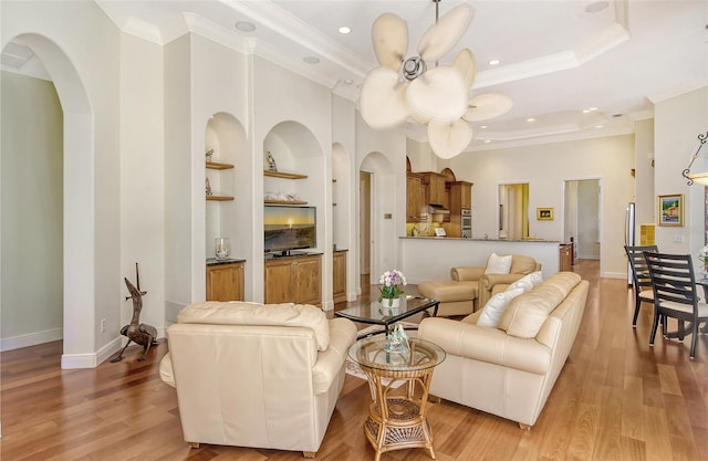 living room featuring a tray ceiling, ceiling fan, built in features, and ornamental molding