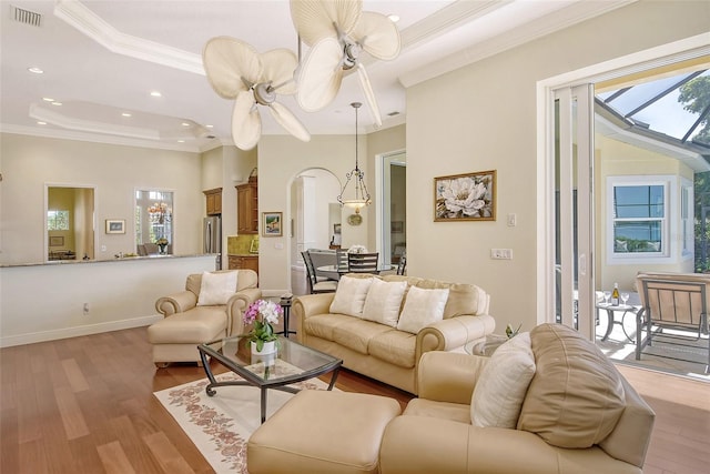 living room with light wood-type flooring, a tray ceiling, and crown molding