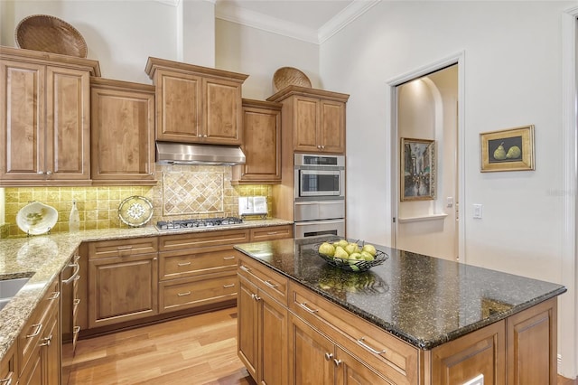 kitchen with decorative backsplash, appliances with stainless steel finishes, light wood-type flooring, and dark stone counters