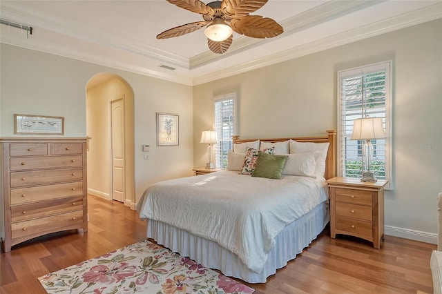 bedroom with ceiling fan, light hardwood / wood-style floors, a raised ceiling, and crown molding