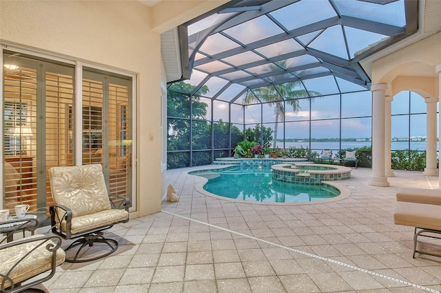 pool at dusk featuring an in ground hot tub, a patio, a water view, and a lanai