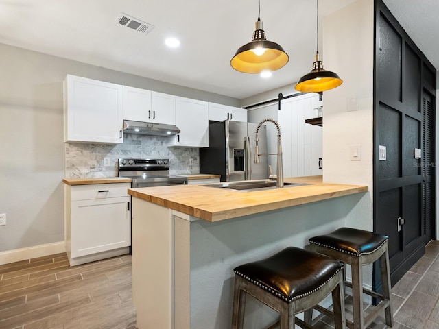 kitchen featuring white cabinetry, stainless steel appliances, a kitchen bar, wood counters, and a barn door