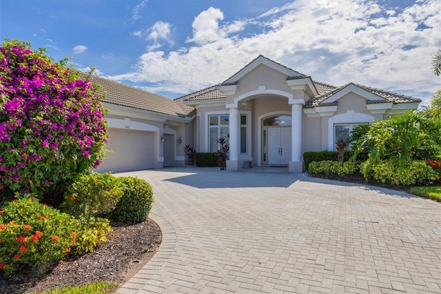 view of front of property with decorative driveway, an attached garage, a tile roof, and stucco siding