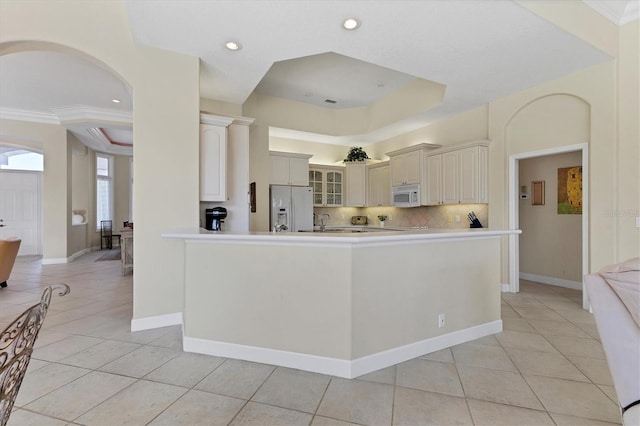 kitchen featuring white appliances, light countertops, a tray ceiling, glass insert cabinets, and tasteful backsplash