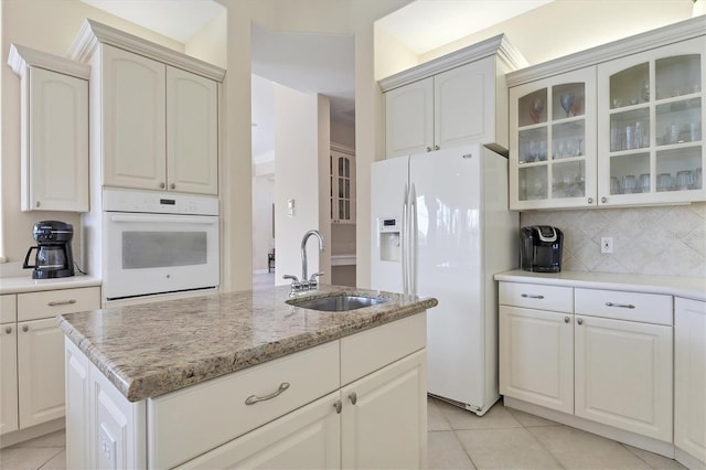 kitchen featuring white appliances, light tile patterned floors, glass insert cabinets, a sink, and backsplash