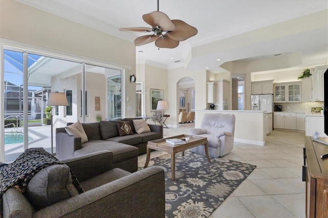 living area featuring arched walkways, ornamental molding, light tile patterned flooring, ceiling fan, and baseboards