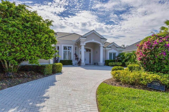 greek revival house featuring decorative driveway, a tile roof, and stucco siding