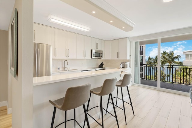 kitchen with kitchen peninsula, appliances with stainless steel finishes, white cabinets, a breakfast bar, and sink