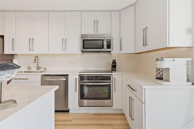 kitchen with light stone countertops, appliances with stainless steel finishes, white cabinetry, sink, and light hardwood / wood-style flooring