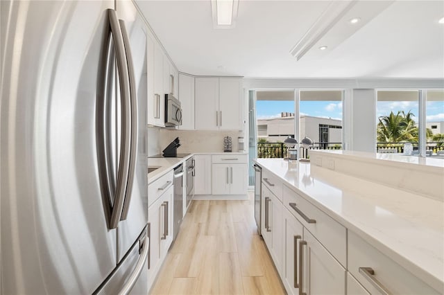 kitchen featuring decorative backsplash, white cabinetry, light wood-type flooring, appliances with stainless steel finishes, and light stone counters