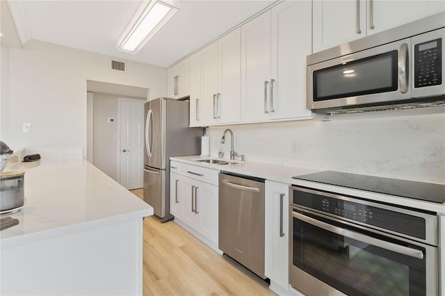 kitchen with white cabinetry, stainless steel appliances, light wood-type flooring, light stone countertops, and sink