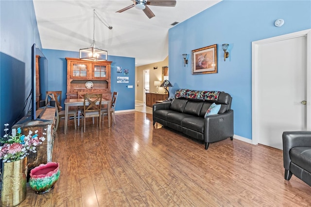 living area featuring lofted ceiling, ceiling fan, wood finished floors, and baseboards