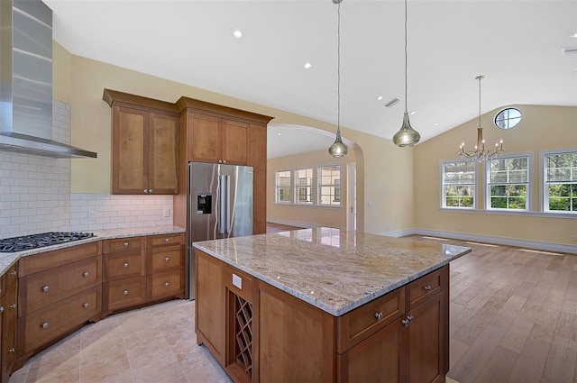 kitchen with a center island, wall chimney range hood, tasteful backsplash, hanging light fixtures, and vaulted ceiling