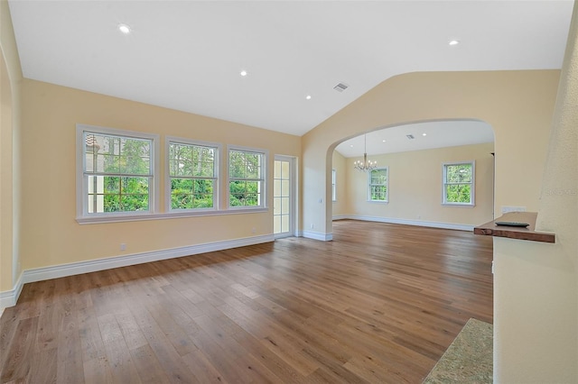 unfurnished living room featuring plenty of natural light, lofted ceiling, a chandelier, and hardwood / wood-style floors