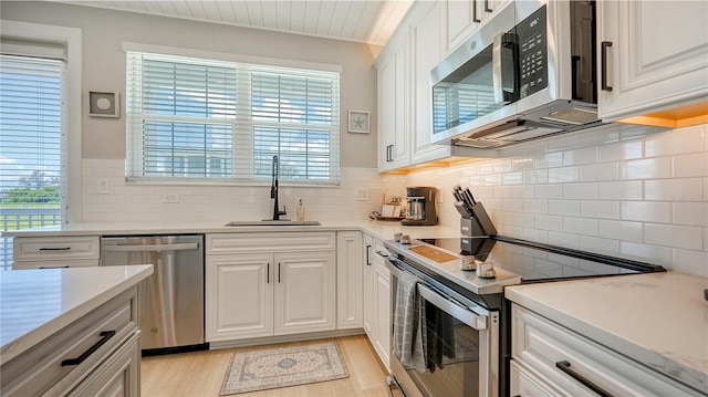 kitchen featuring white cabinetry, tasteful backsplash, light hardwood / wood-style floors, appliances with stainless steel finishes, and sink