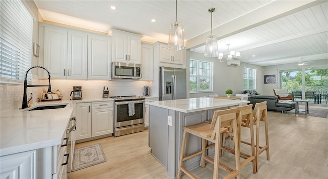 kitchen with appliances with stainless steel finishes, sink, light stone counters, light wood-type flooring, and beam ceiling