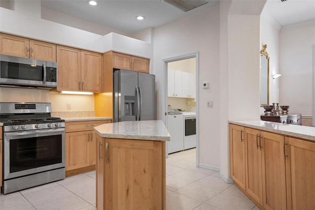 kitchen with washer and clothes dryer, light tile patterned floors, light stone counters, a kitchen island, and appliances with stainless steel finishes