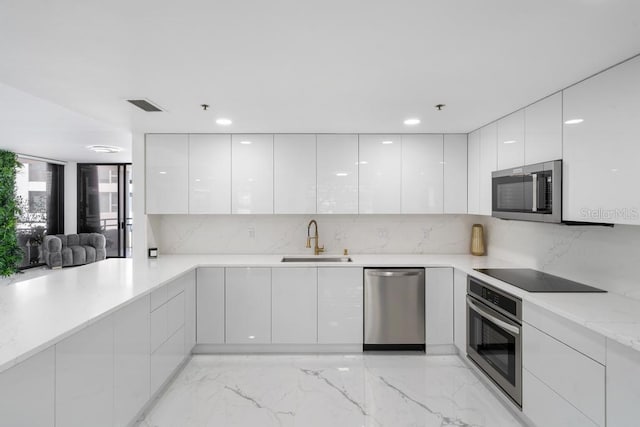 kitchen with sink, appliances with stainless steel finishes, light stone counters, white cabinets, and decorative backsplash