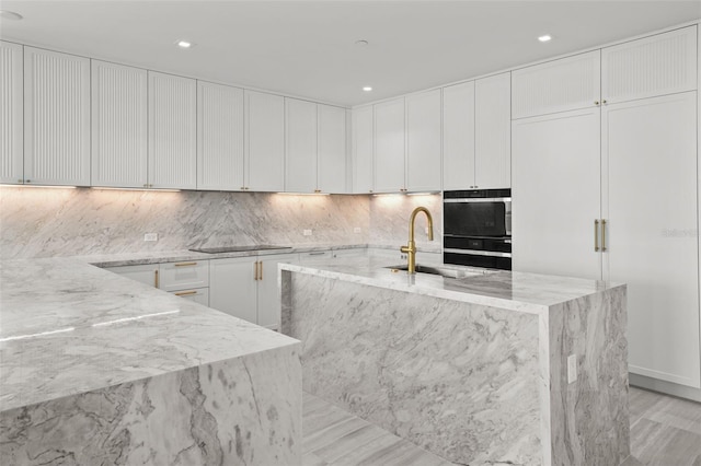 kitchen featuring sink, white cabinets, decorative backsplash, a kitchen island with sink, and light stone counters