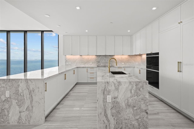 kitchen featuring a water view, white cabinetry, black oven, and an island with sink